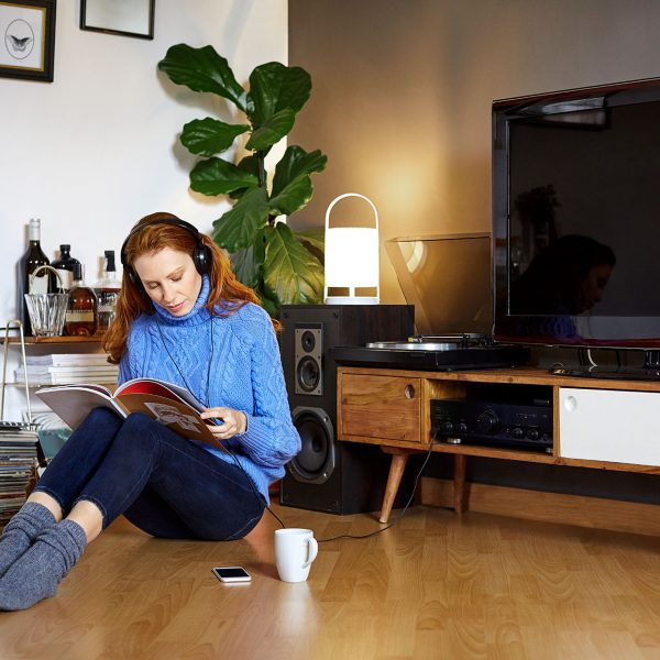 Eine Frau sitzt auf dem Fu&szlig;boden und liest in einem Magazin, hinter ihr sind ein Sideboard mit TV-Ger&auml;t und Lautsprechern rechts und links zu sehen.