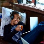 Eine Person liegt auf einem Sofa, h&auml;lt eine Tasse in der Hand und videotelefoniert &uuml;ber ein Notebook.
