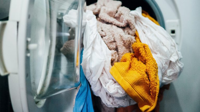 Aus einer Waschmaschine hängen einige Handtücher und Teile von Bettwäsche heraus.