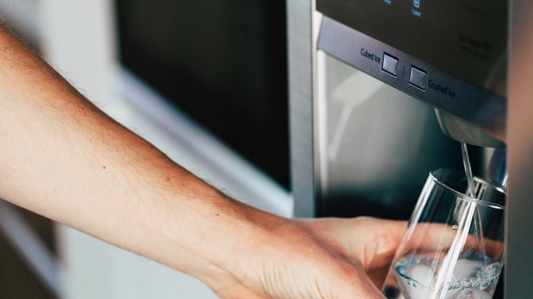Eine Person hält ein Glas unter einen Wasserstrahl, der aus einem Side-by-Side-Kühlschrank kommt.