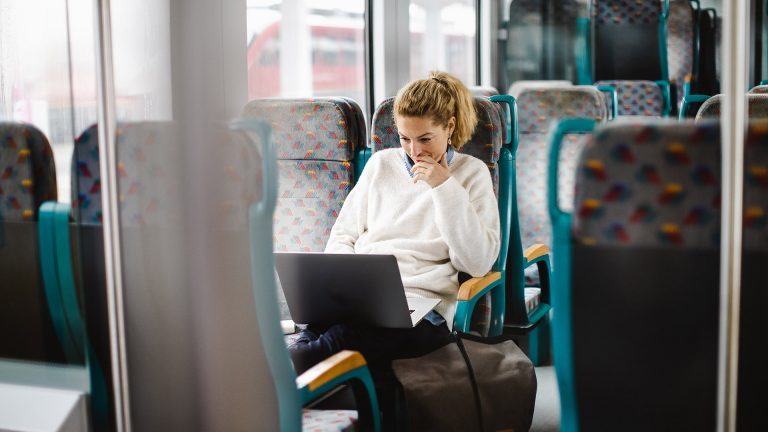 Eine Person sitzt in der Bahn und hat einen Laptop auf dem Scho&szlig;.