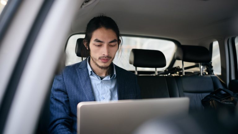 Eine Person arbeitet mit einem Laptop auf dem Rücksitz in einem Auto.