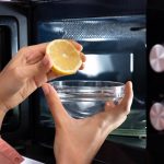 Eine Person träufelt den Saft einer Zitrone in eine Schüssel mit Wasser, ehe sie diese in die Mikrowelle gibt.