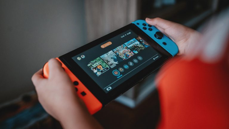 Eine Person hält eine Nintendo Switch in der Hand und schaut die Spiele im Hauptmenü an.