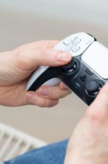 Eine Person hält einen DualSense-Controller der PS5 in Weiß in der Hand.