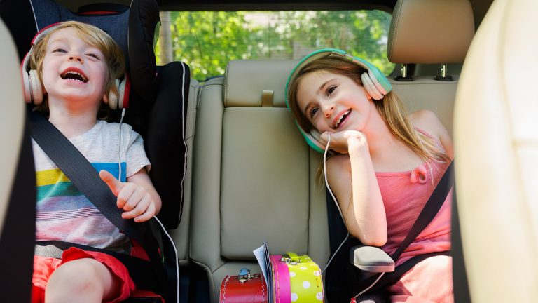 Zwei Kinder mit Kopfhörern auf den Ohren sitzen auf der Rückbank eines Autos