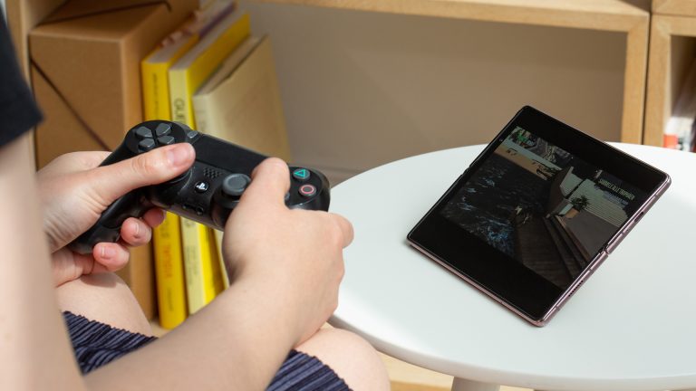 Eine Person hält einen PS4-Controller in der Hand und spielt auf einem Samsung Galaxy Z Fold2 ein Spiel.