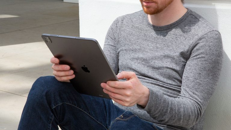 Ein junger Mann lehnt an einer Hauswand, in den Händen hält er ein iPad.