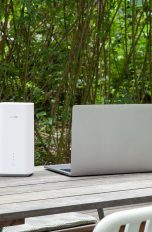 Ein Huawei GigaCube 5G steht auf einem Terrassen-Tisch im Garten neben einem Notebook.