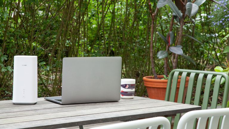 Ein Huawei GigaCube 5G steht auf einem Terrassen-Tisch im Garten neben einem Notebook.