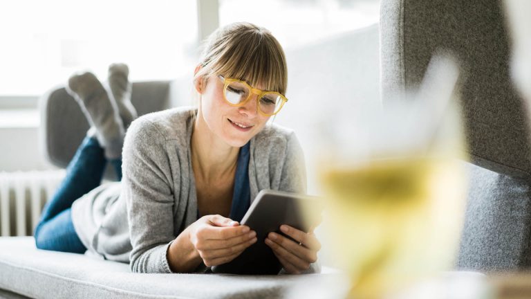 Eine Person liegt auf einem Sofa und schaut auf ein iPad.