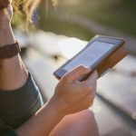 Eine Person sitzt im Freien und h&auml;lt einen E-Book-Reader in der Hand.