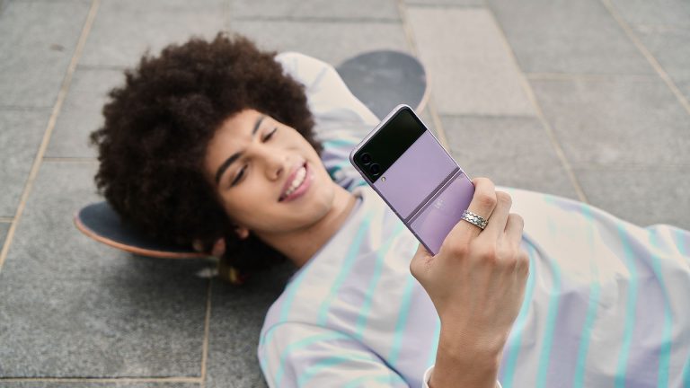 Eine Person liegt auf dem Boden. In der Hand hält sie ein aufgeklapptes Samsung Galaxy Z Flip3 5G.