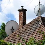 Zwei Satellitenschüsseln auf dem Dach eines älteren Hauses.