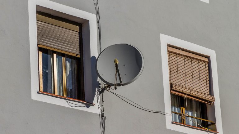 Eine Satellitenschüssel hängt nahe eines Fensters an einem Haus.