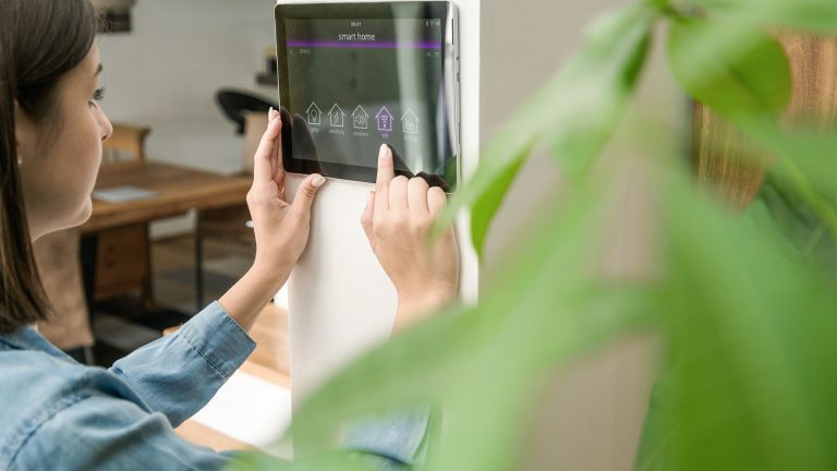 Eine Person steuert Smarthome-Funktionen über ein an der Wand montiertes Tablet.