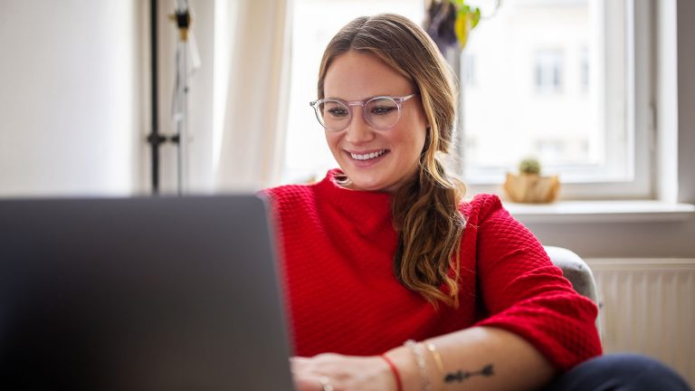 Eine Person sitzt auf einem Sofa und schaut in einen Laptop.