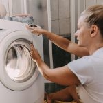 Eine Person sitzt vor einer Waschmaschine und bedient sie.