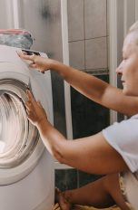 Eine Person sitzt vor einer Waschmaschine und bedient sie.