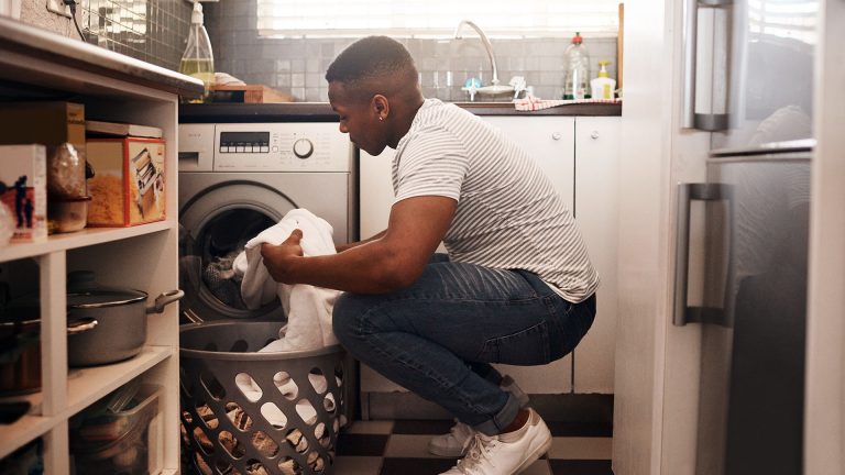 Eine Person holt Wäsche aus einer Waschmaschine.