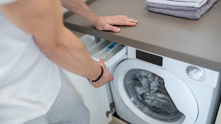 Eine Person öffnet das Waschmittelfach an einer Waschmaschine und schaut hinein.