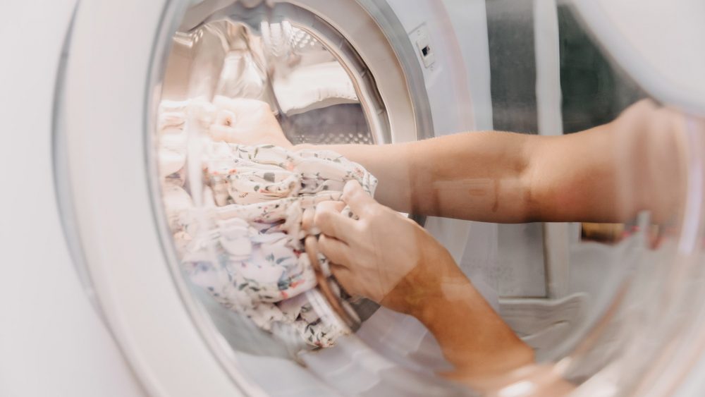 Eine Person holt Wäsche aus der Trommel einer Waschmaschine.