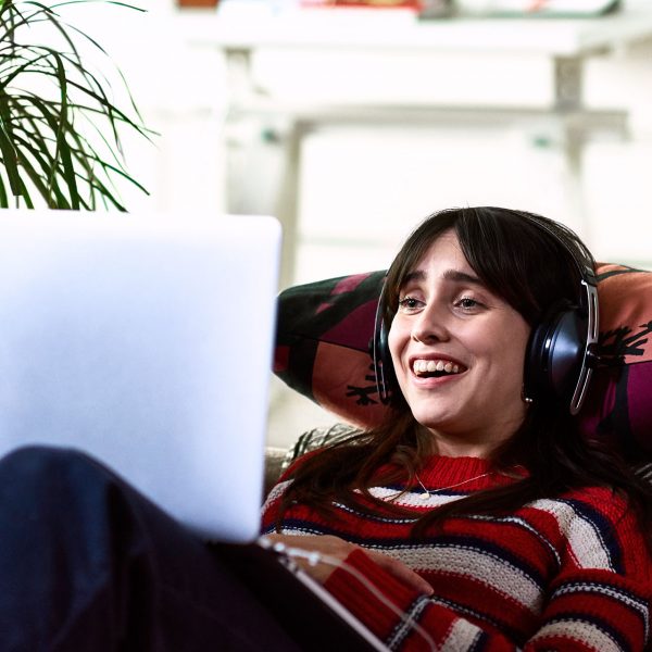 Eine Person liegt auf dem Sofa, hat Kopfh&ouml;rer auf und schaut in einen Laptop.
