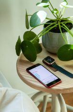 Eine Apple Watch und ein iPhone liegen nebeneinander auf einem Nachttisch.