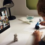 Ein Kind sitzt vor einem iPad, auf dem ein FaceTime-Call mit mehreren Teilnehmern läuft, und bemalt Figuren.