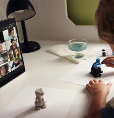 Ein Kind sitzt vor einem iPad, auf dem ein FaceTime-Call mit mehreren Teilnehmern läuft, und bemalt Figuren.