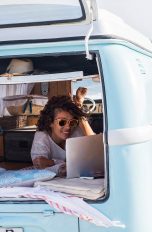 Eine Person in einem Kleinbus campt am Meer und surft mit einem Notebook im Internet.