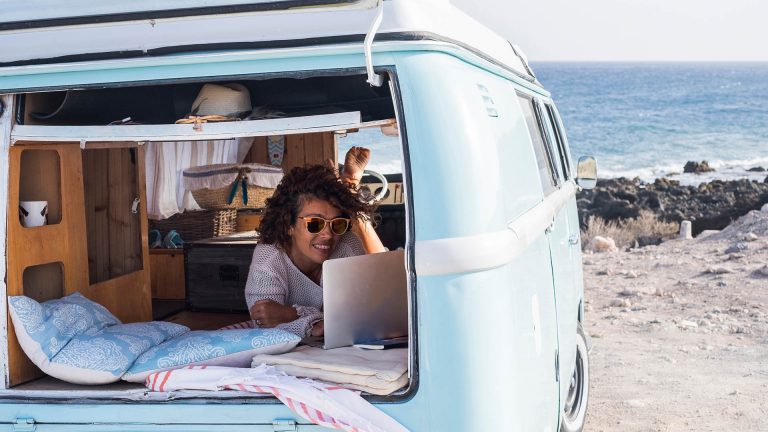 Eine Person in einem Kleinbus campt am Meer und surft mit einem Notebook im Internet.