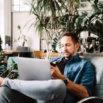 Eine Person sitzt entspannt auf einem Sessel, hat einen Laptop auf dem Scho&szlig; und ein Smartphone in der Hand.