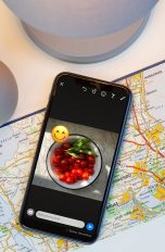 Ein iPhone liegt auf einer Landkarte. Auf dem Bildschirm ist das Foto einer Speise zu sehen, das über WhatsApp als Story geteilt werden soll.