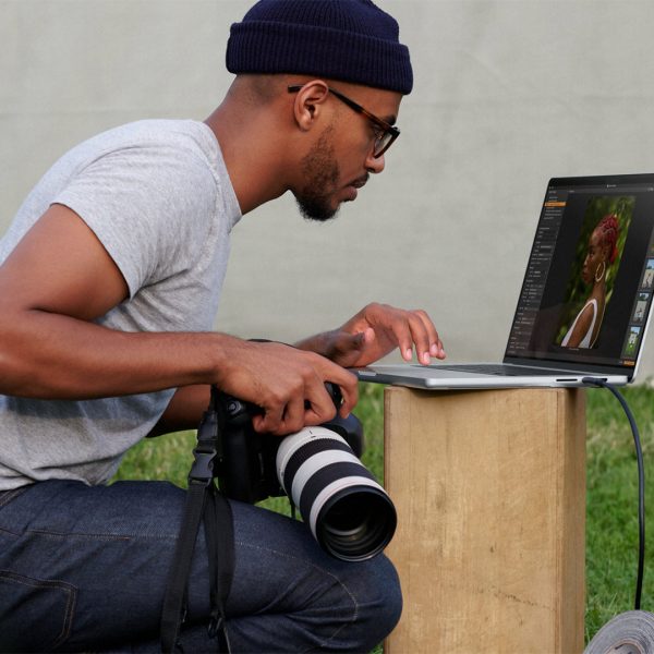 Eine Person mit einer Kamera in der Hand betrachtet die geschossenen Bilder auf einem MacBook Pro.