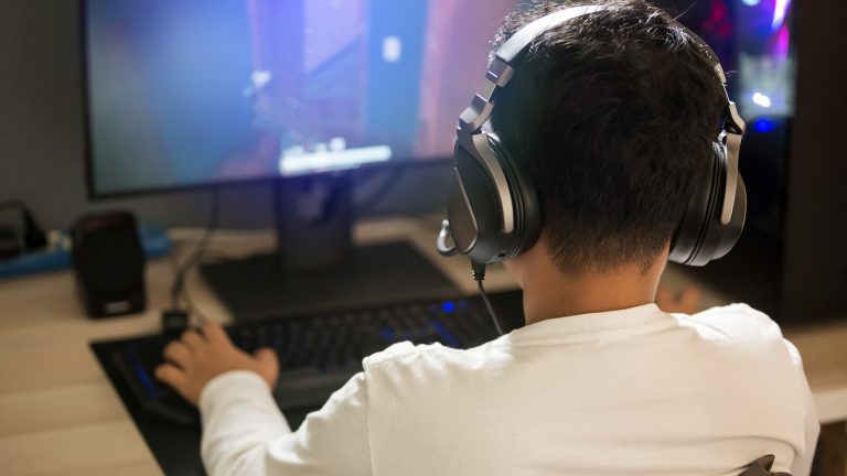 Eine Person mit einem Headset auf dem Kopf sitzt vor einem Rechner und spielt etwas.