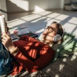Eine Person liegt auf dem Boden, liest etwas und hört dabei Musik über Kopfhörer.