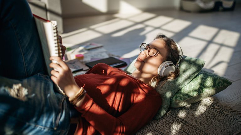 Eine Person liegt auf dem Boden, liest etwas und hört dabei Musik über Kopfhörer.