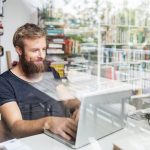 Eine Person sitzt an einem Laptop und tippt. Im Hintergrund sind B&uuml;cherregale zu sehen.