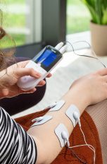Eine Person wendet ein TENS-Ger&auml;t am Arm an.