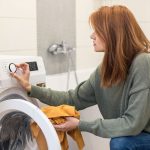 Eine Person f&uuml;llt W&auml;sche in eine Waschmaschine und stellt das Programm ein.