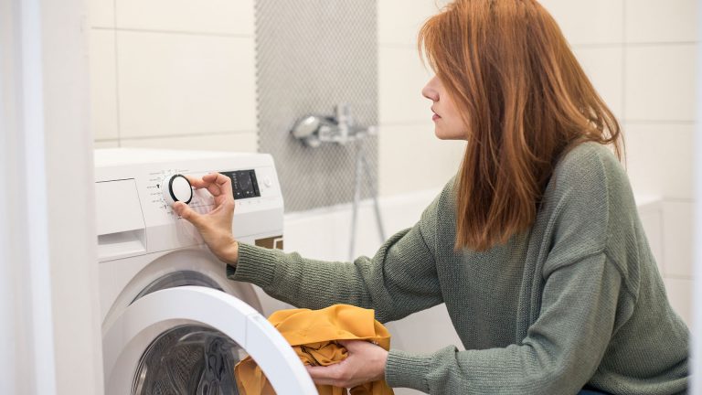 Eine Person füllt Wäsche in eine Waschmaschine und stellt das Programm ein.