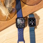 Eine Apple Watch 7 liegt neben einer Apple Watch SE auf einem Holztisch neben einigen Deko-Elementen.