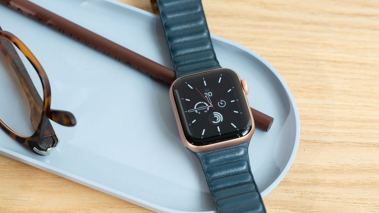 Eine Apple Watch SE liegt eingeschaltet neben einer Brille in einer Schale.