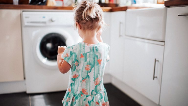 Ein Kind steht in einer Küche vor einer Waschmaschine.