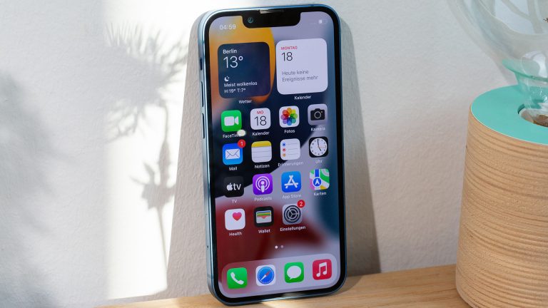 Ein iPhone 13 Mini steht, gegen eine Wand gelehnt, auf einem Sideboard.
