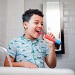 Ein Kind steht vor einem Waschbecken und putzt sich die Zähne mit einer elektrischen Zahnbürste.