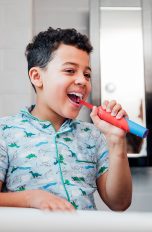 Ein Kind steht vor einem Waschbecken und putzt sich die Zähne mit einer elektrischen Zahnbürste.