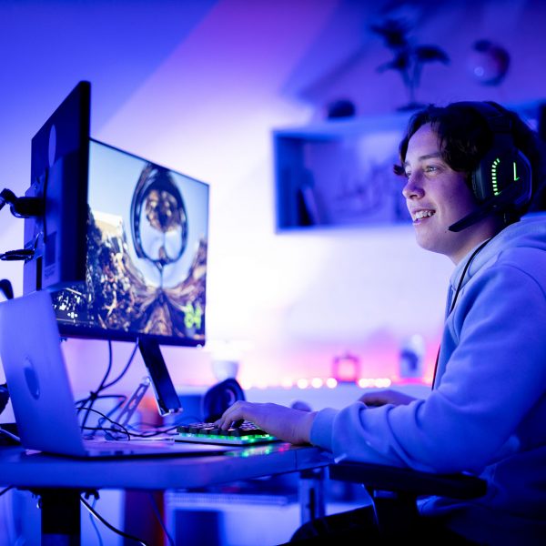 Eine Person spielt an einem Tisch, auf dem ein Laptop und zwei Monitore stehen.