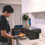 Ein Person stellt ein St&uuml;ck Pizza in eine Mikrowelle.